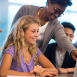 Three students in a row. Professor leans over one and points at her computer screen.