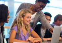 Three students in a row. Professor leans over one and points at her computer screen.
