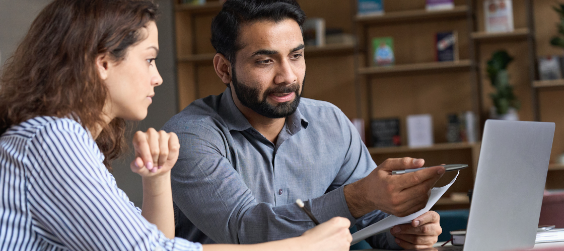 A professor and student sit in front of an open laptop, discussing what's on the screen.