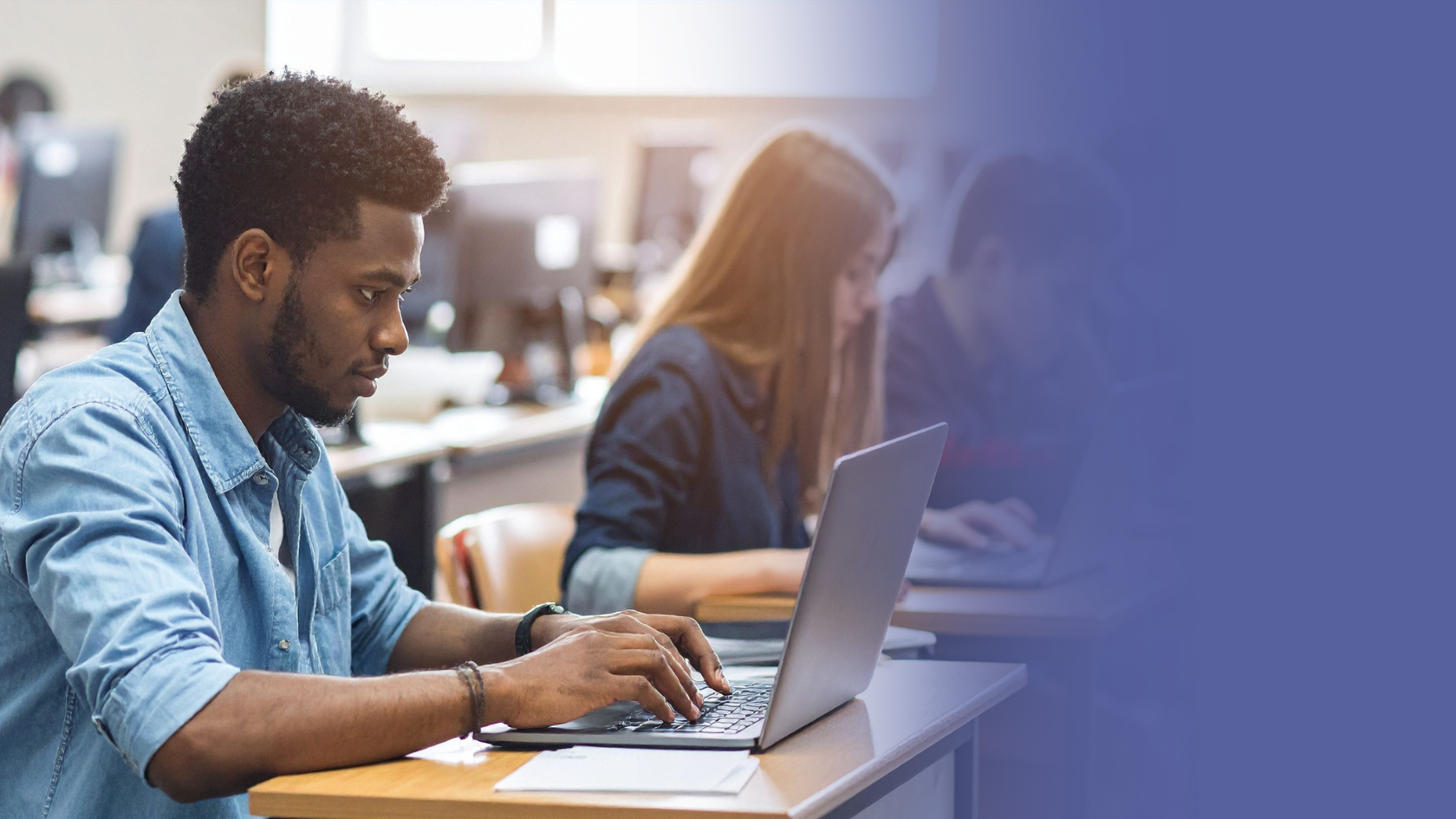 Male student sits at desk and works with laptop
