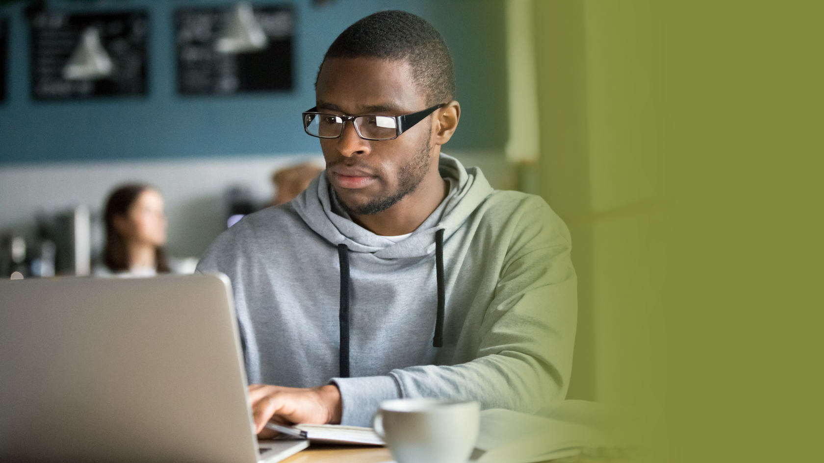 A man with glasses and a hoodie works at a laptop computer
